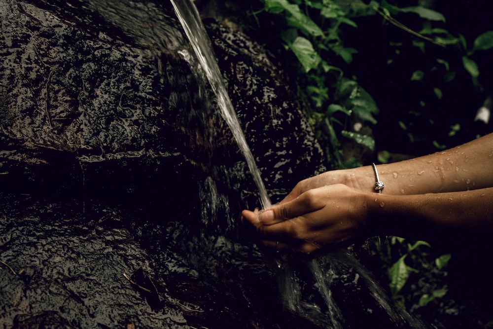 A woman's hands cupping a stream of water flowing from a rock.